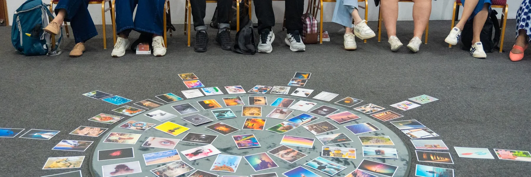A full deck of picture cards laid out in a circle on the floor with participants seated around it